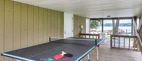 Une table de ping-pong avec deux raquettes, installée sur une terrasse en bois offrant une vue sur un lac.