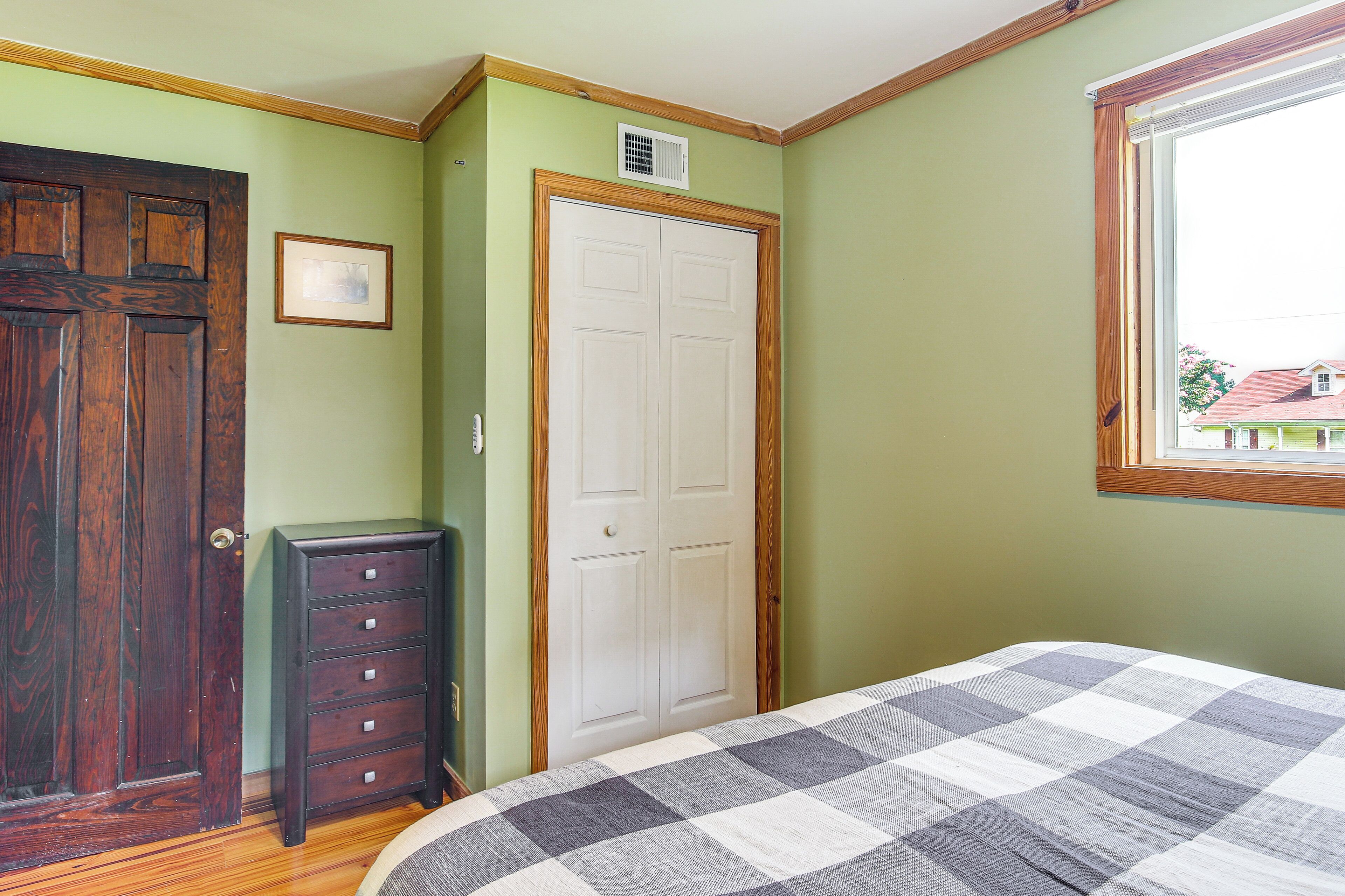 A bedroom with a wooden door, a white closet, a dresser, and a checkered bedspread.