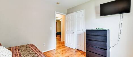 A bedroom with a bed, a dresser, a ceiling fan, and a TV on the wall.