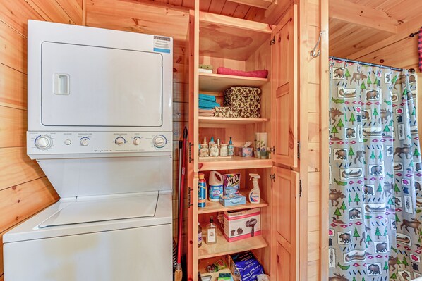 A compact kitchen with a white stove, a wooden cabinet with various kitchen items, and a patterned shower curtain. - Serene Cabin < 1 Mi to Fairy Stone State Park! (Stuart)