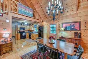 A wooden cabin interior with a dining area, kitchen, and a large chandelier.