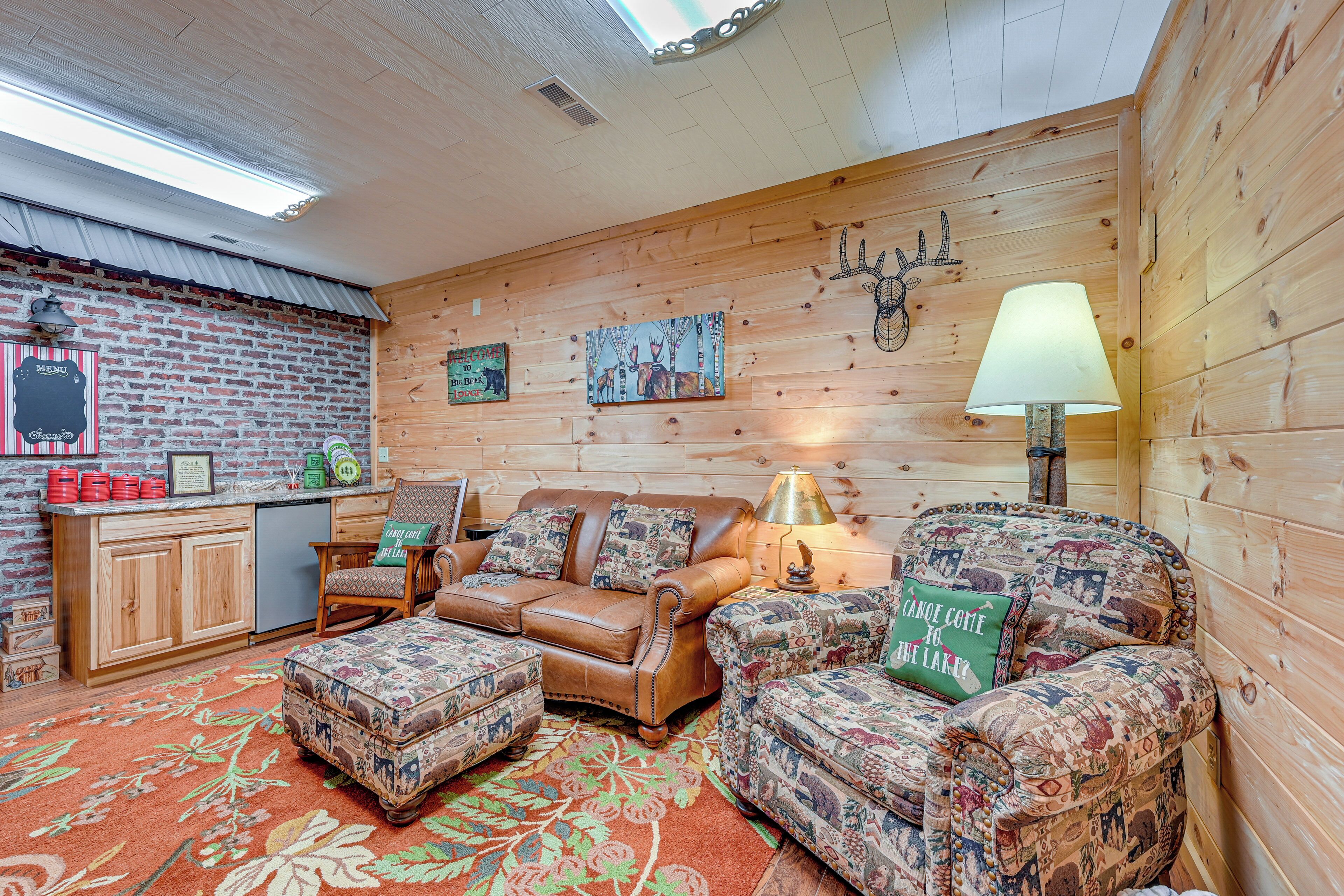 A cozy cabin interior with a wooden interior, a sofa, a chair, a small table, and a lamp.