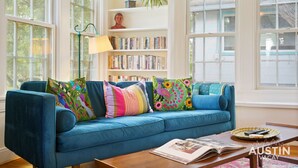 Una sala de estar con un sofá azul, almohadones coloridos, una estantería y una lámpara.