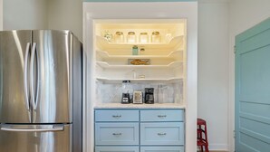 Una cocina con un refrigerador de acero inoxidable, una repisa empotrada con frascos, una cafetera y un tostador.