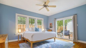 Un dormitorio con cama, ventilador de techo, ventana y vista al exterior.