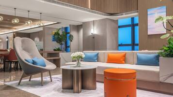 A modern lobby with a seating area, a round table with a vase, and a large window.