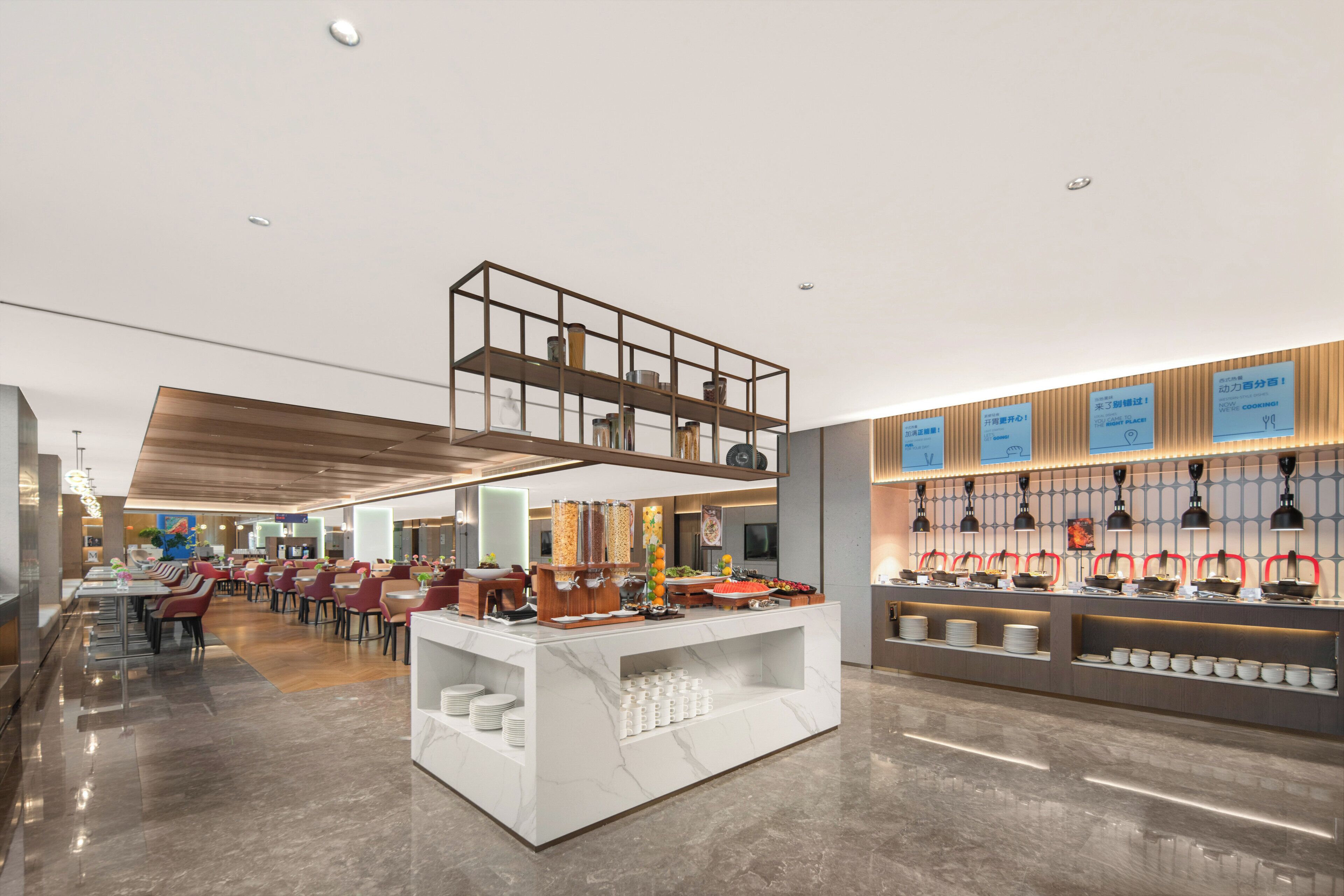 A modern hotel lobby with a buffet area, seating arrangements, and a reception desk.