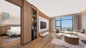 Une chambre d’hôtel moderne dotée d’un grand lit, d’un téléviseur fixé au mur, d’un coin salon avec une table basse et offrant une vue sur la ville grâce à de grandes fenêtres.