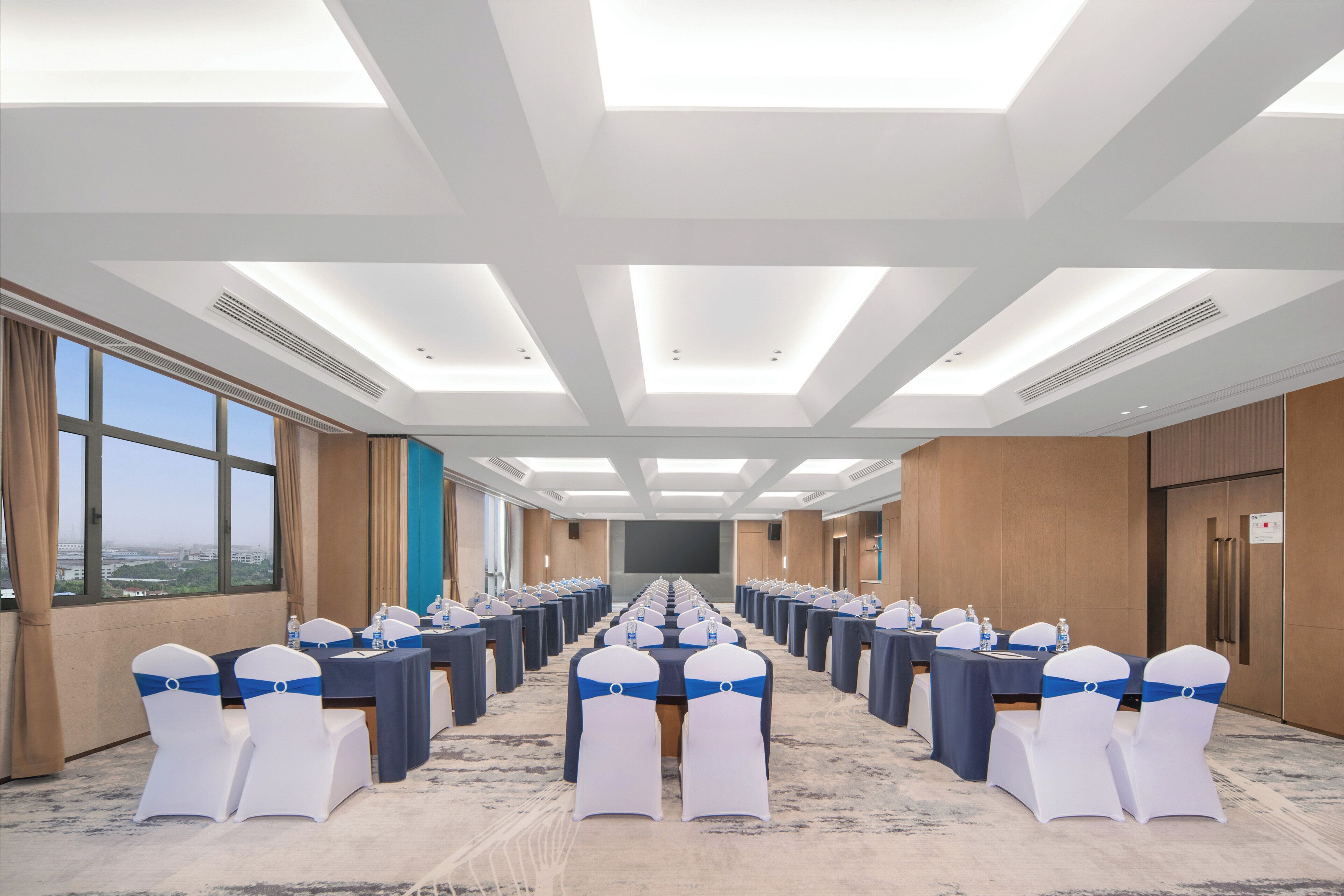 A conference room with a long table, chairs with blue sashes, and a large screen at the front.