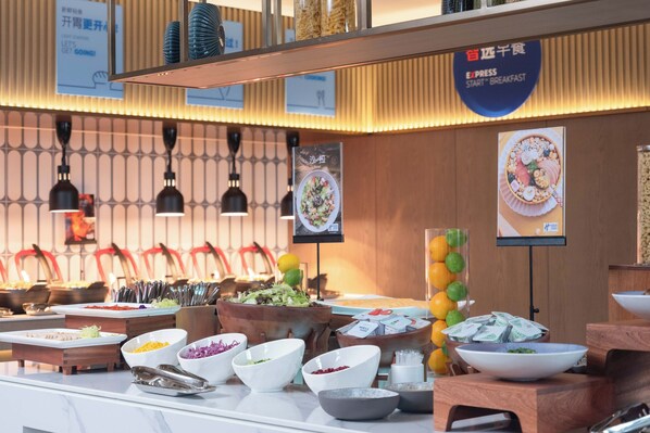 A buffet area with various food stations, including bowls of salad, fruits, and other dishes. There are signs indicating breakfast options and a sign for 'Express Breakfast'. - Holiday Inn Express Wuxi Xishan by IHG (Wuxi)
