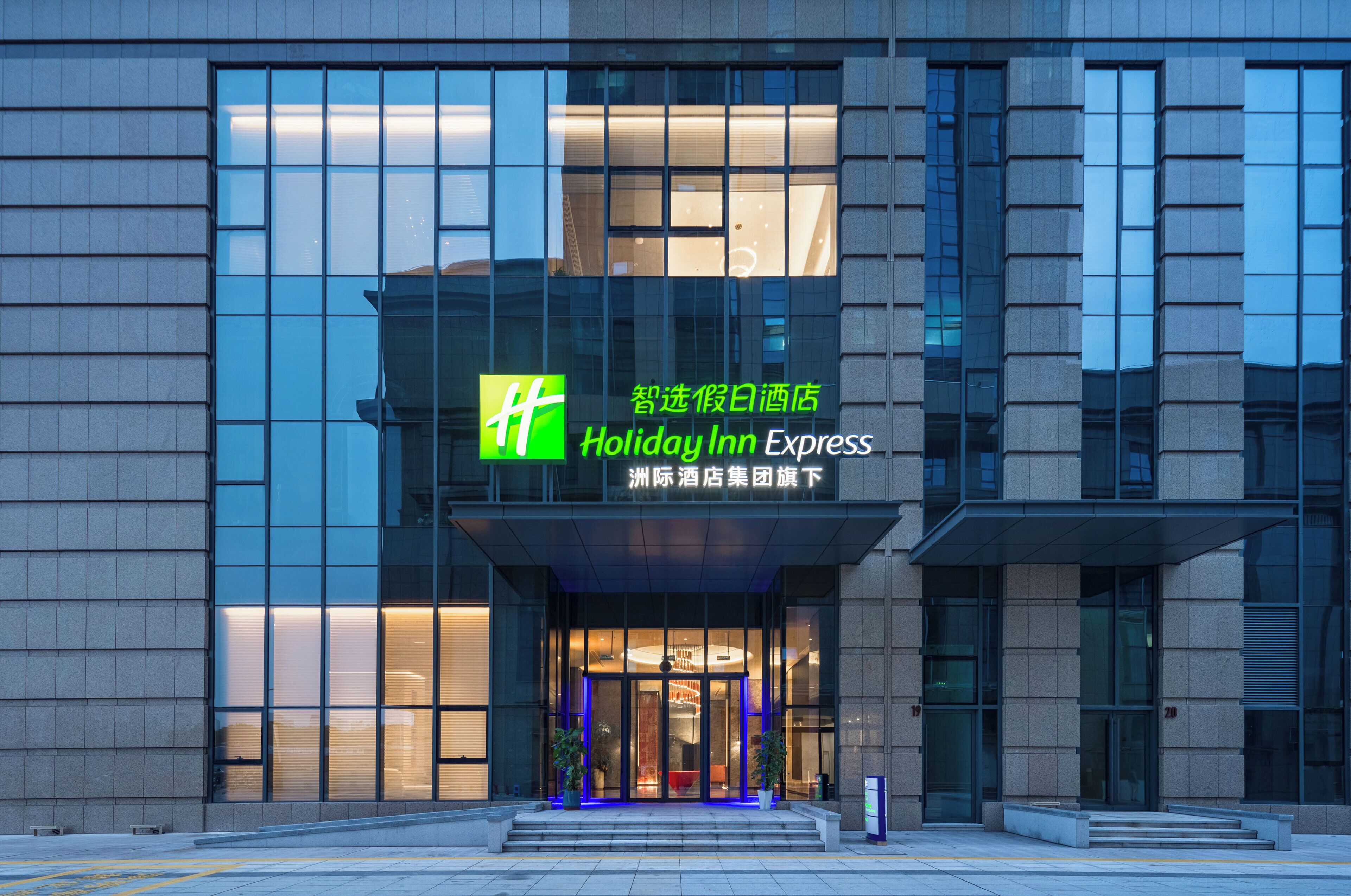 Edificio Holiday Inn Express con fachada de vidrio moderna y una entrada destacada con escalones ascendentes.