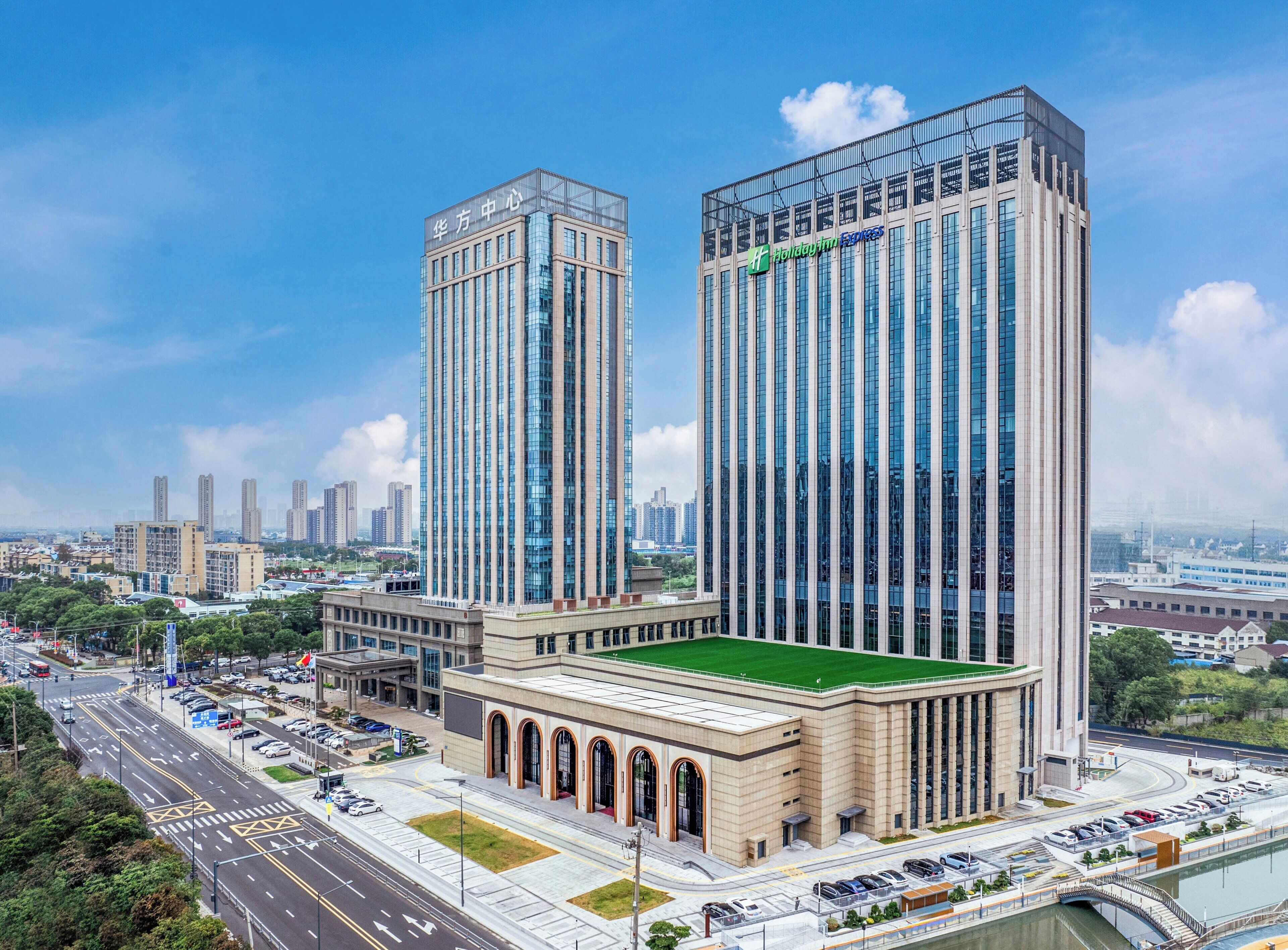 A modern hotel with two tall towers, a green-roofed building, and a view of the surrounding cityscape.