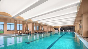 Une grande piscine intérieure à l’eau d’un bleu limpide, avec un plafond baigné de lumière naturelle et des espaces aménagés le long des bords pour s’asseoir.