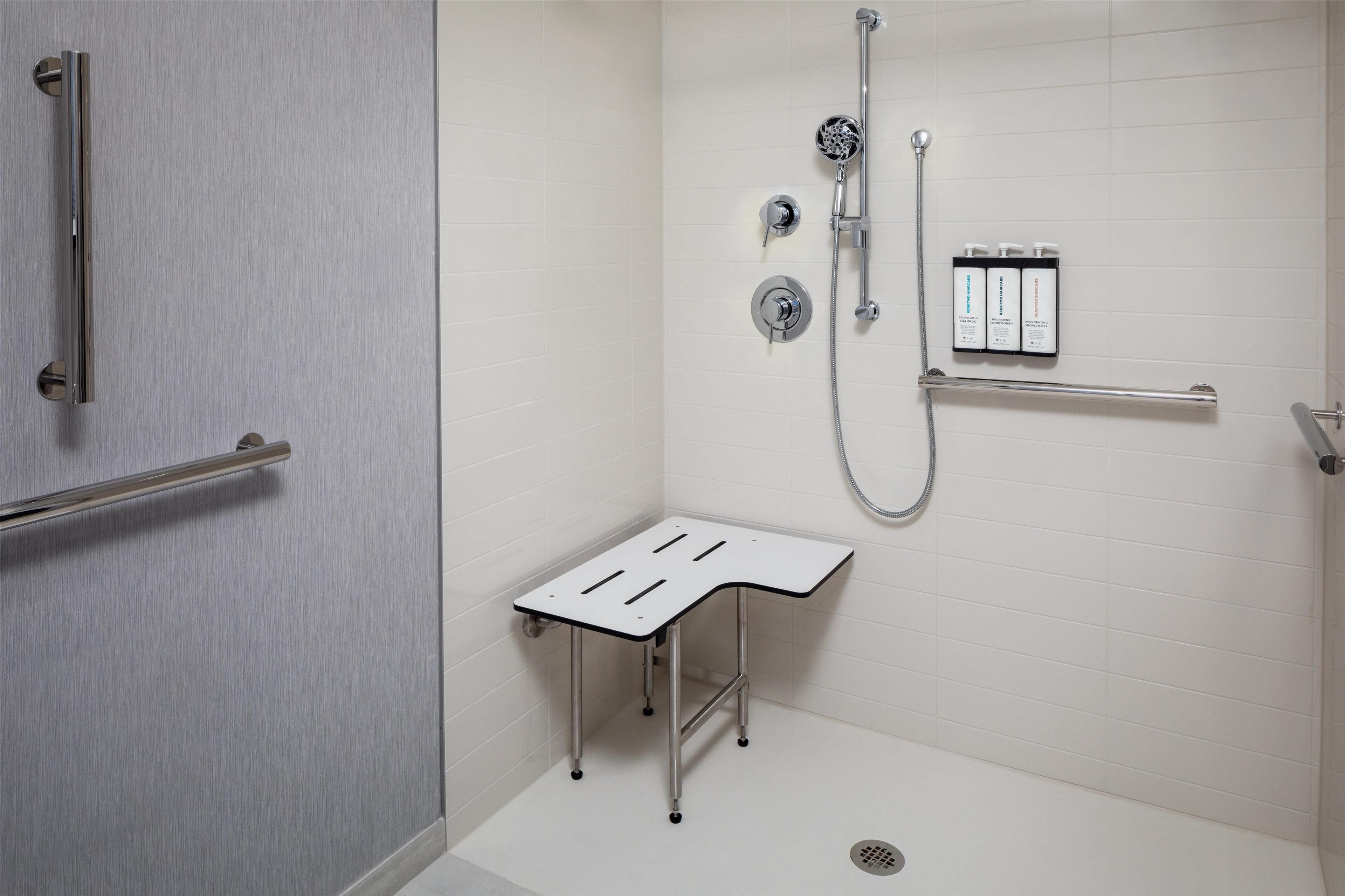 Un baño moderno con ducha, barra de apoyo y una mesita.