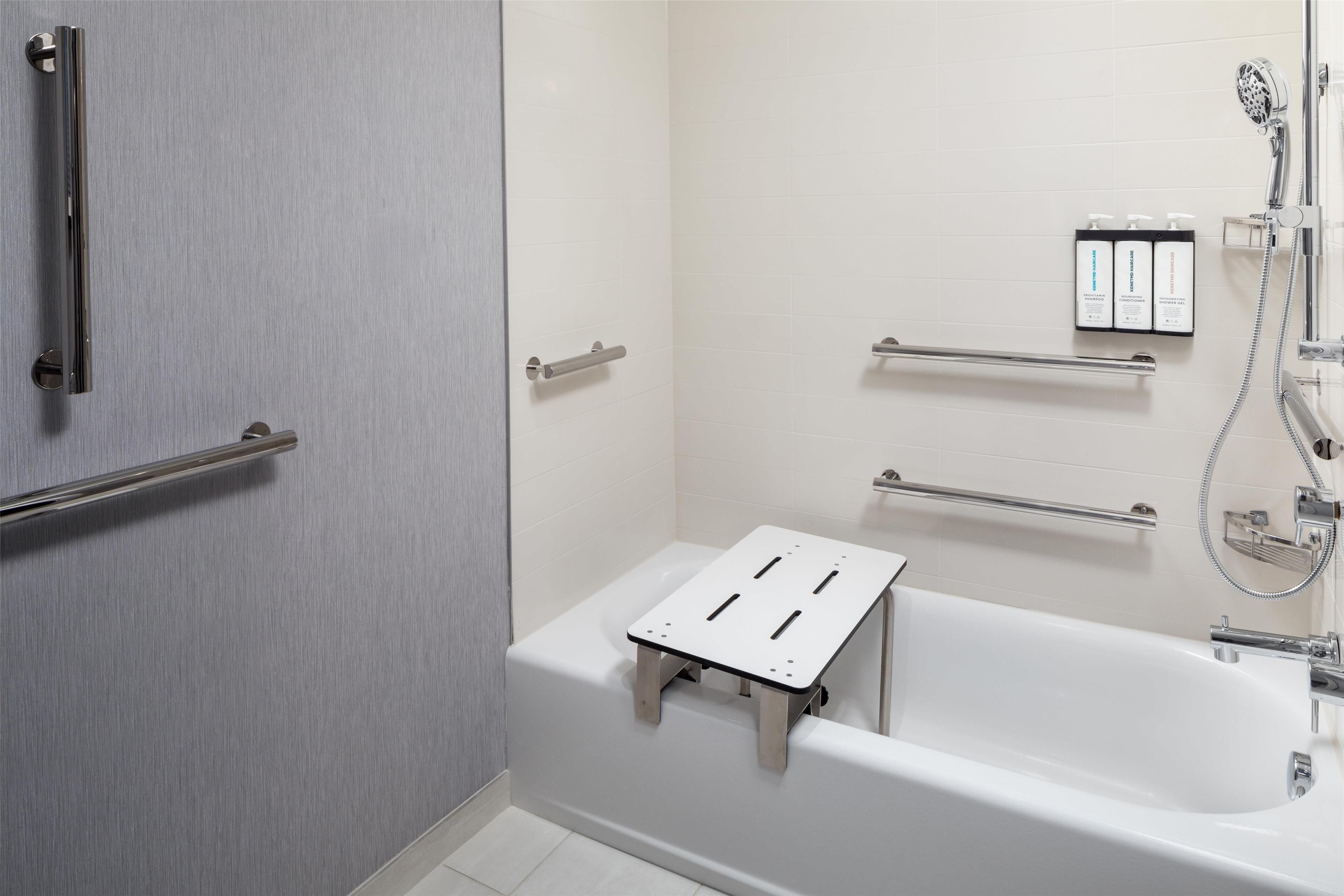 A modern bathroom with a walk-in shower, grab bars, a white bathtub, and a shelf with toiletries.