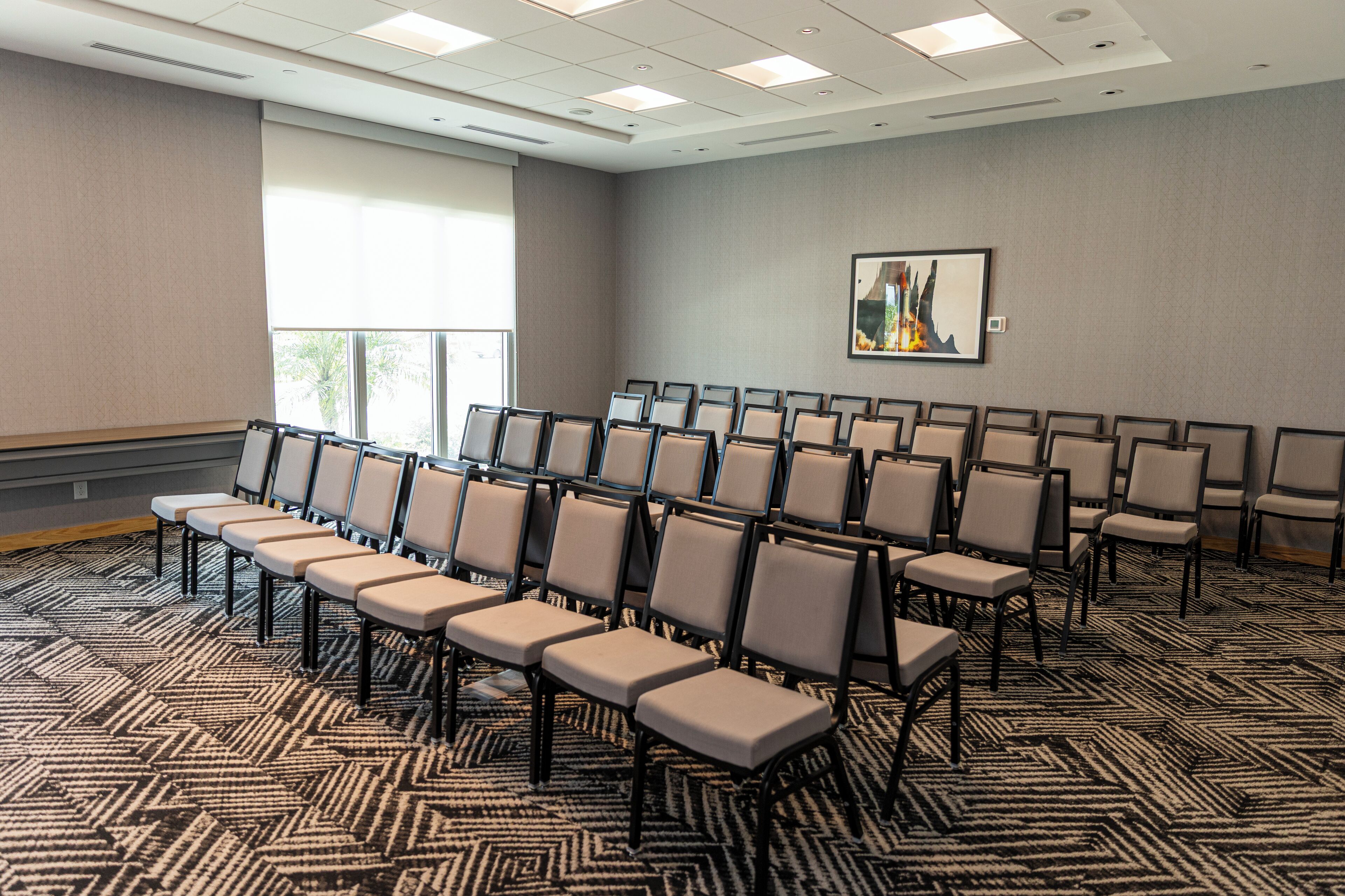 A conference room with rows of chairs, a patterned carpet, and a large window.