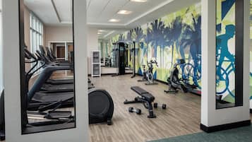 Un gimnasio con cintas de correr, máquinas de pesas y un espejo grande.