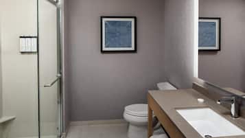 A modern bathroom with a glass shower enclosure, a white toilet, a beige vanity with a sink, and two framed wall art pieces.