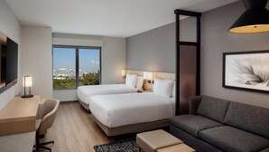 Una camera d'albergo moderna con due letti, una scrivania, un divano e un'ampia finestra con vista sulla città.