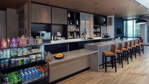 A modern bar area with a long counter, bar stools, and shelves stocked with beverages and snacks. - Hyatt Place Cape Canaveral (Cape Canaveral)