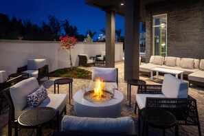 An outdoor patio area with a fire pit, seating, and a view of the city skyline at dusk.