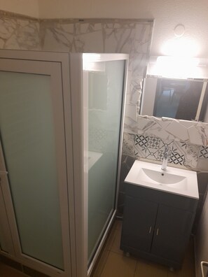 A bathroom with a glass shower enclosure, a sink with a mirror above it, and a tiled backsplash. - Villabadlou Ti-Cocon (Goyave)