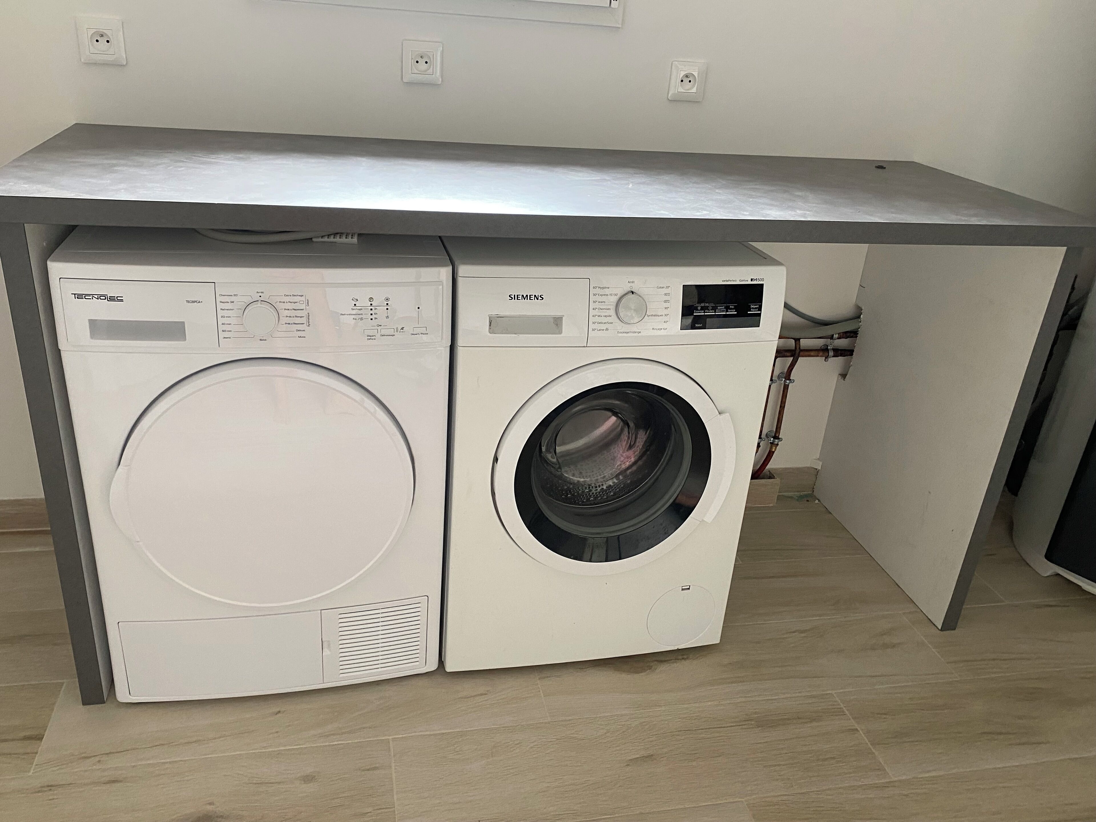 Ein kleiner Waschbereich mit zwei Unterschubwaschmaschinen unter einer grauen Arbeitsplatte.