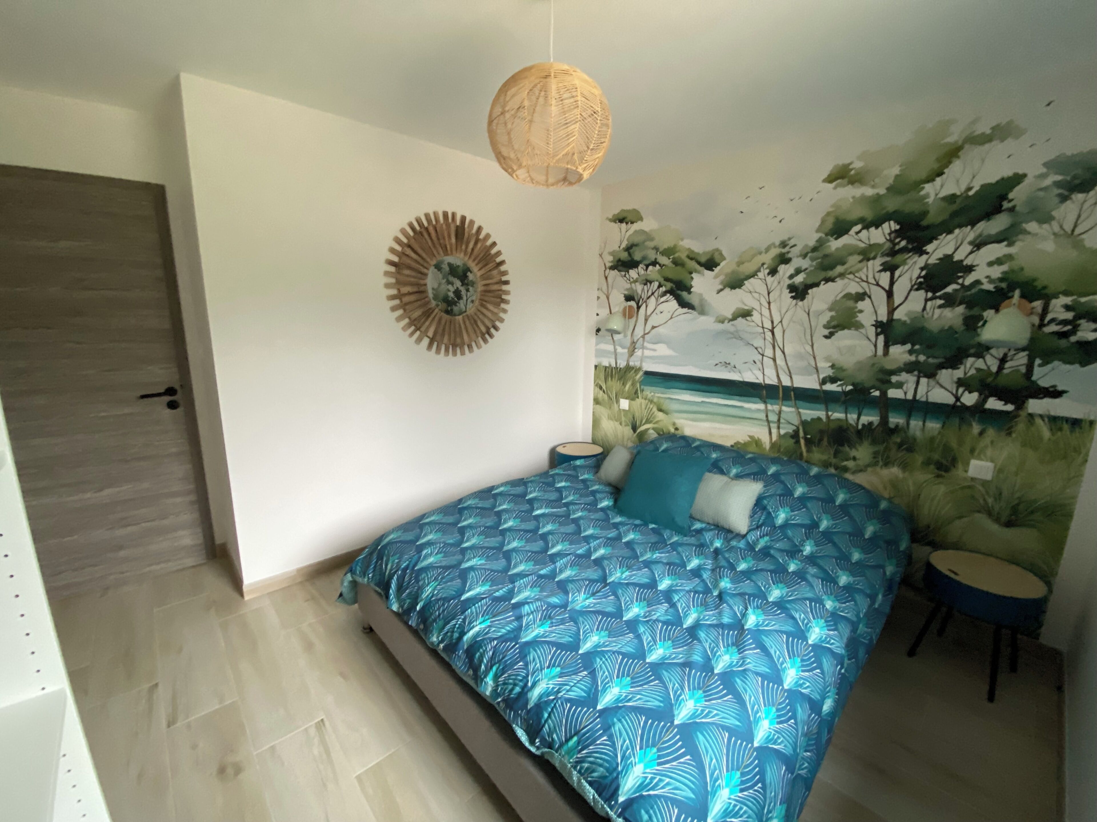 A bedroom with a bed, a wall-mounted lamp, a door, and a mural of a beach scene.