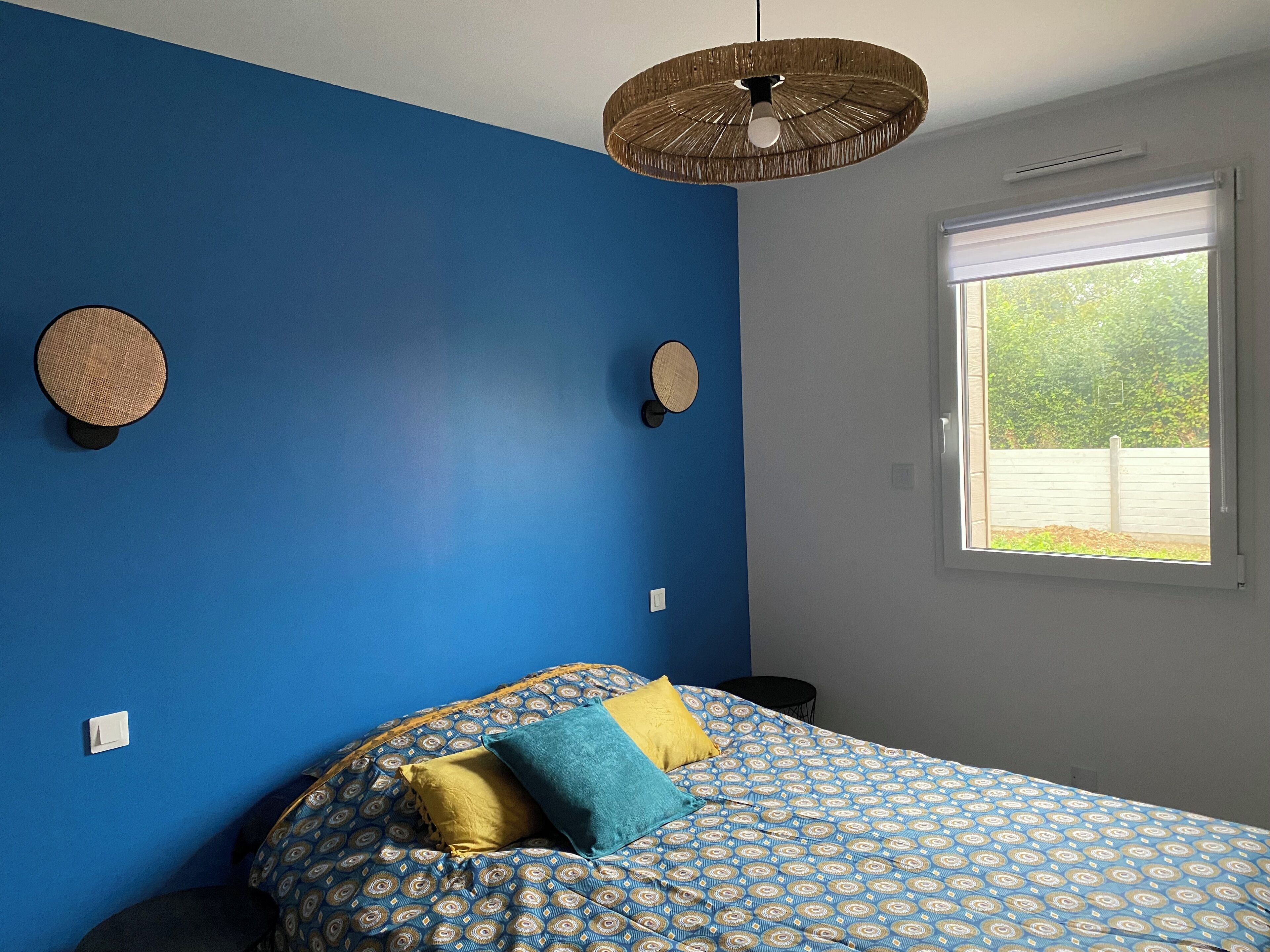 Ein Schlafzimmer mit Bett, Fenster und Wand mit einer runden Dekoration.