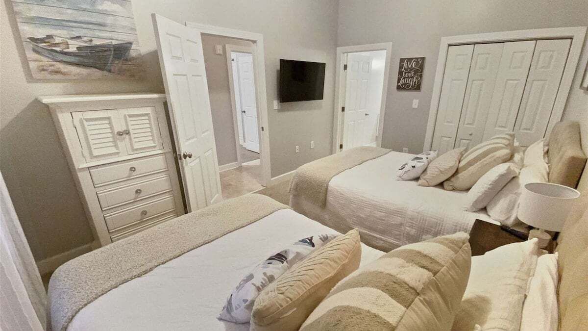 A bedroom with two beds, a TV mounted on the wall, and a painting above the door.