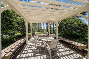 Un patio exterior con una pérgola, mesas, sillas y un banco.