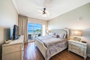 Un dormitorio con una cama grande, ventilador de techo, televisor, mesita de noche y vistas al exterior.