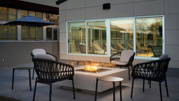An outdoor seating area with wicker chairs and a central fire feature, surrounded by large windows. - Element by Marriott Fort Smith (Fort Smith)