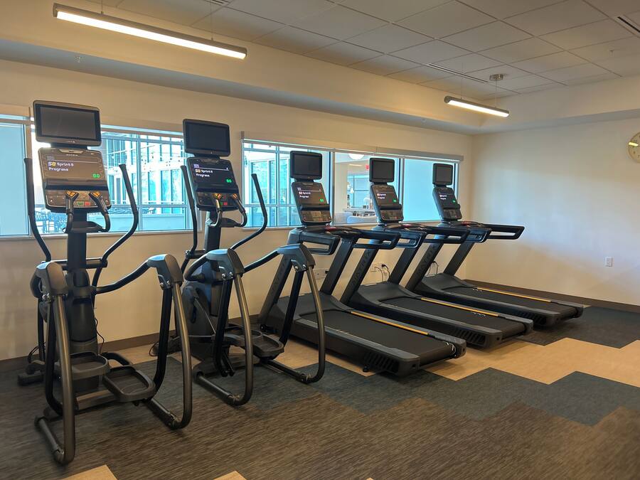 Ett gym med löpband, crosstrainers och motionscyklar, utrustat med digitala skärmar och styrketräningsmaskiner.