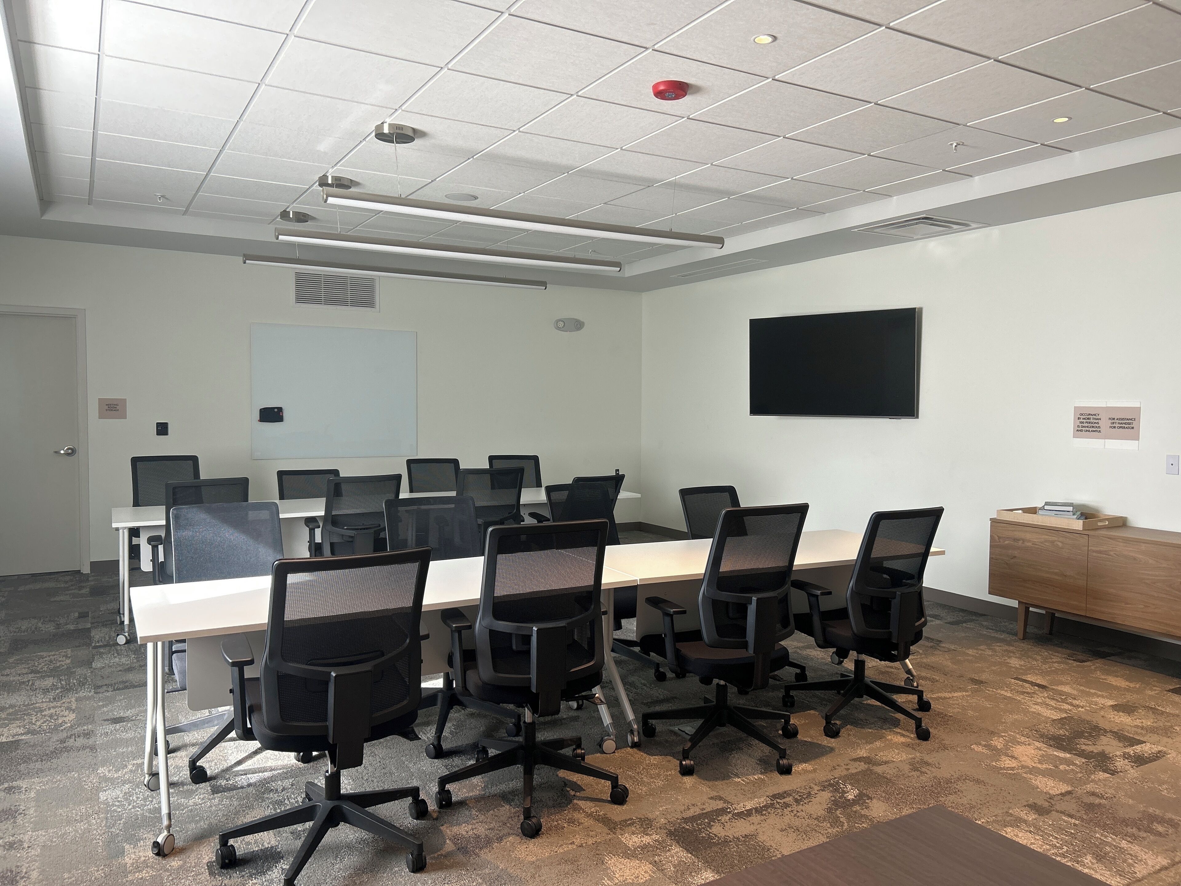 A conference room with a long table, multiple chairs, a whiteboard, and a mounted TV.