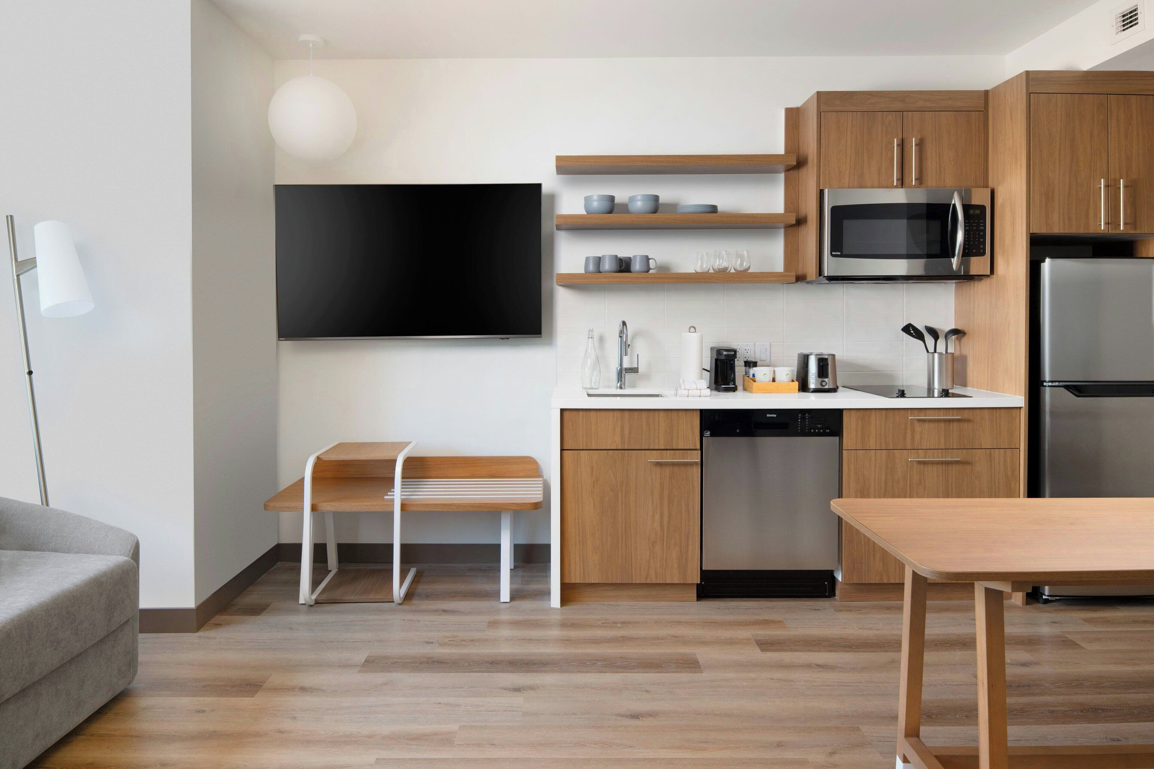 Una cocina moderna con armarios de madera, microondas integrado, refrigerador y un comedor con banco y mesa.