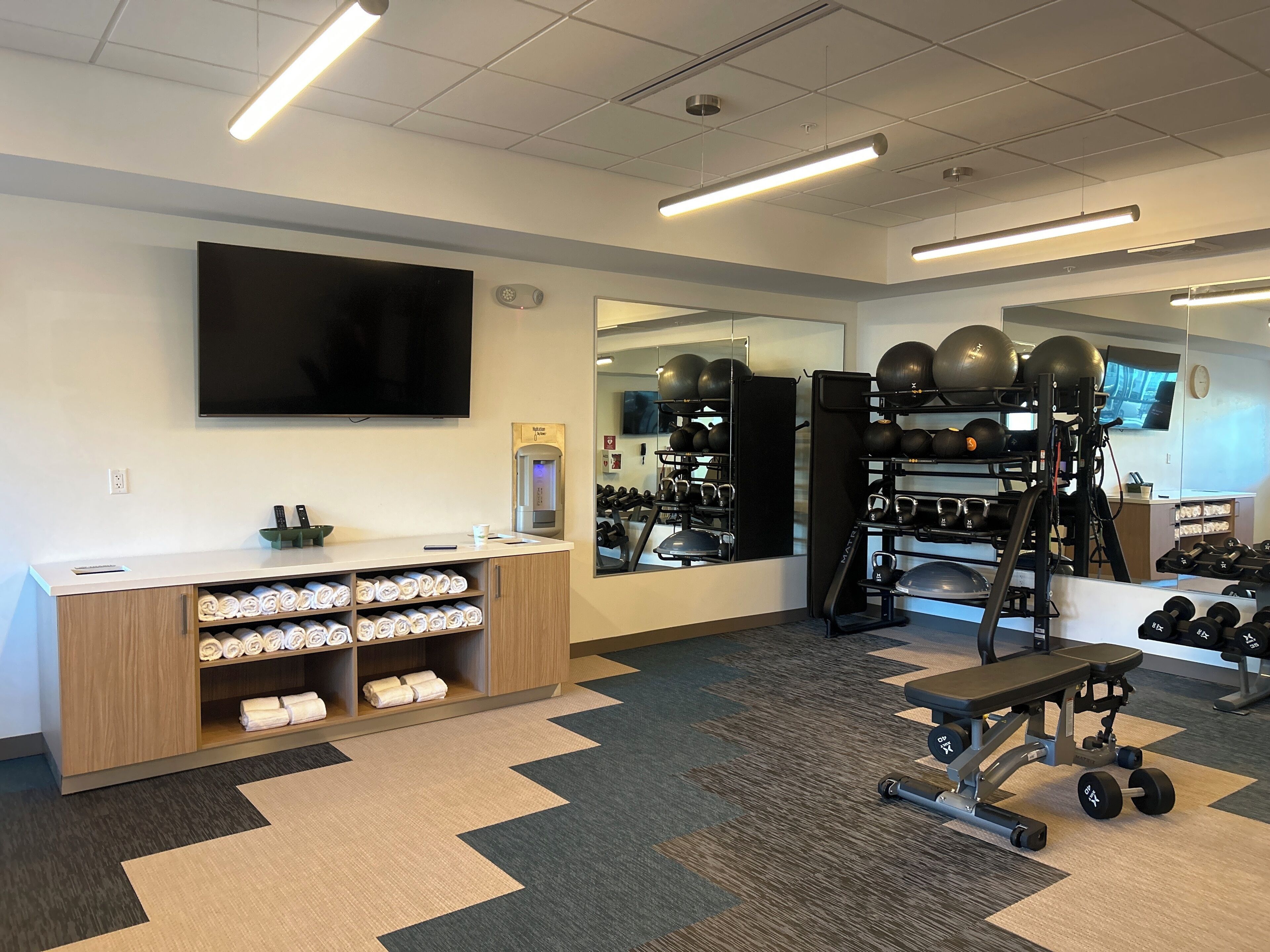 A gym with exercise equipment, a water dispenser, and a TV on the wall.