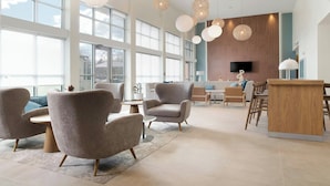 A spacious lobby with large windows, modern furniture, and a wooden reception desk. - Element by Marriott Fort Smith (Fort Smith)