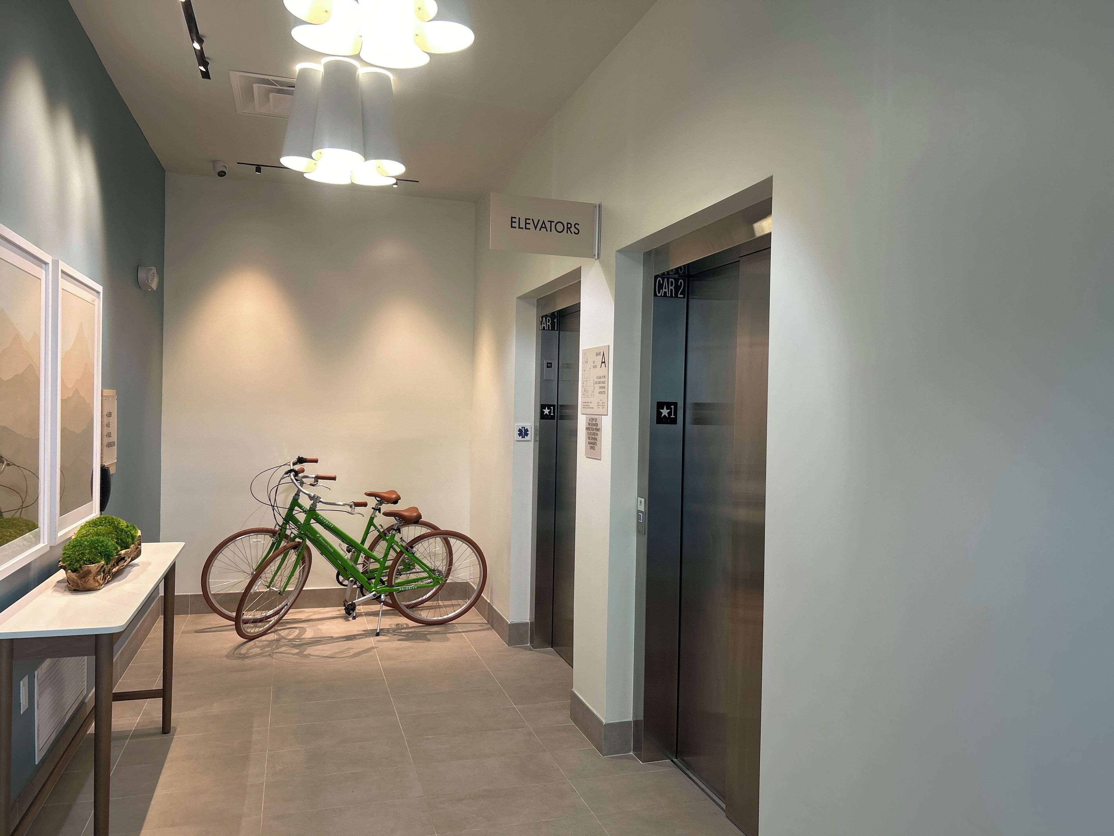 Un couloir avec un ascenseur, un panneau indiquant « Ascenseurs », et un vélo vert appuyé contre le mur.