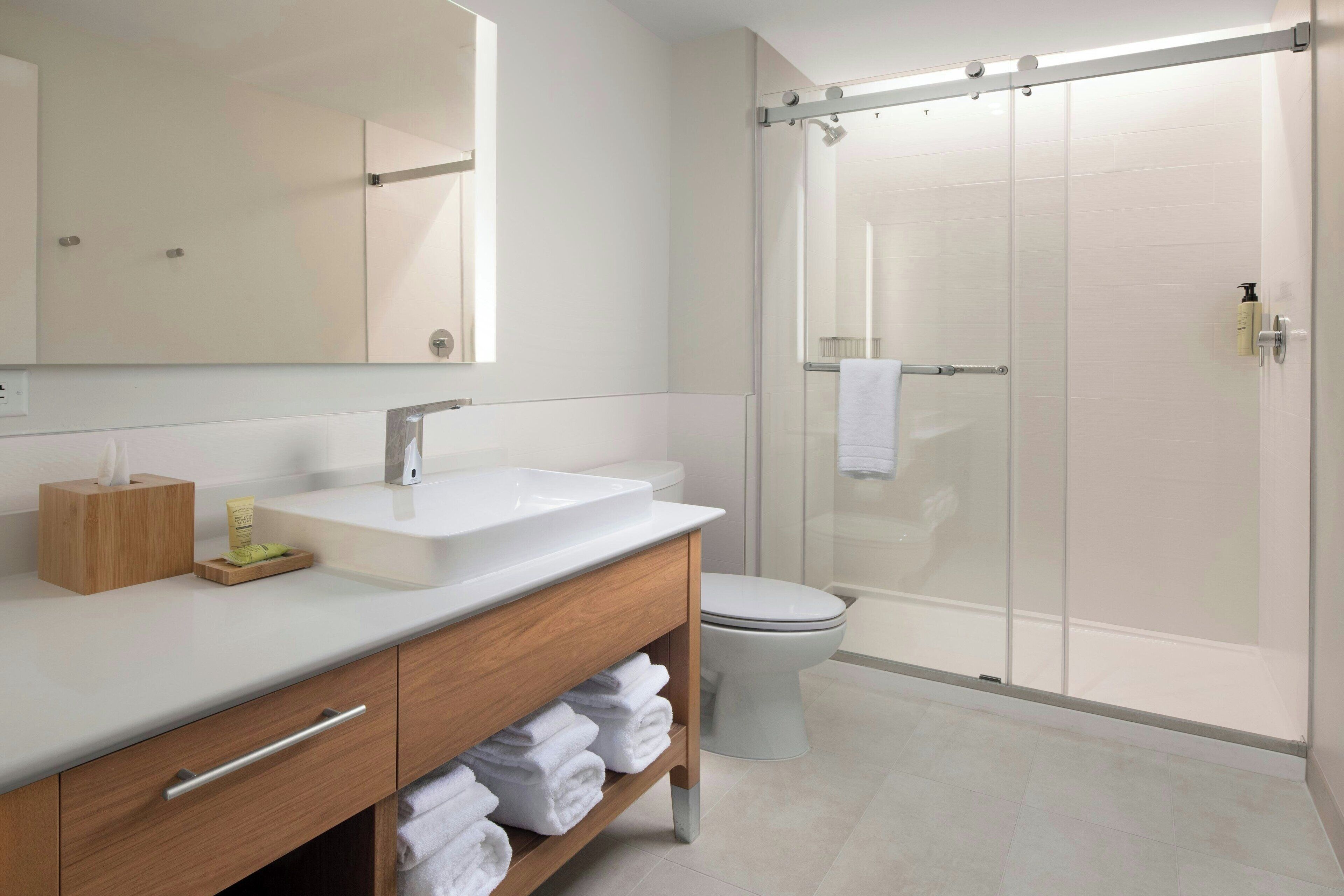 A modern bathroom with a white sink, wooden vanity, and a glass-enclosed shower.