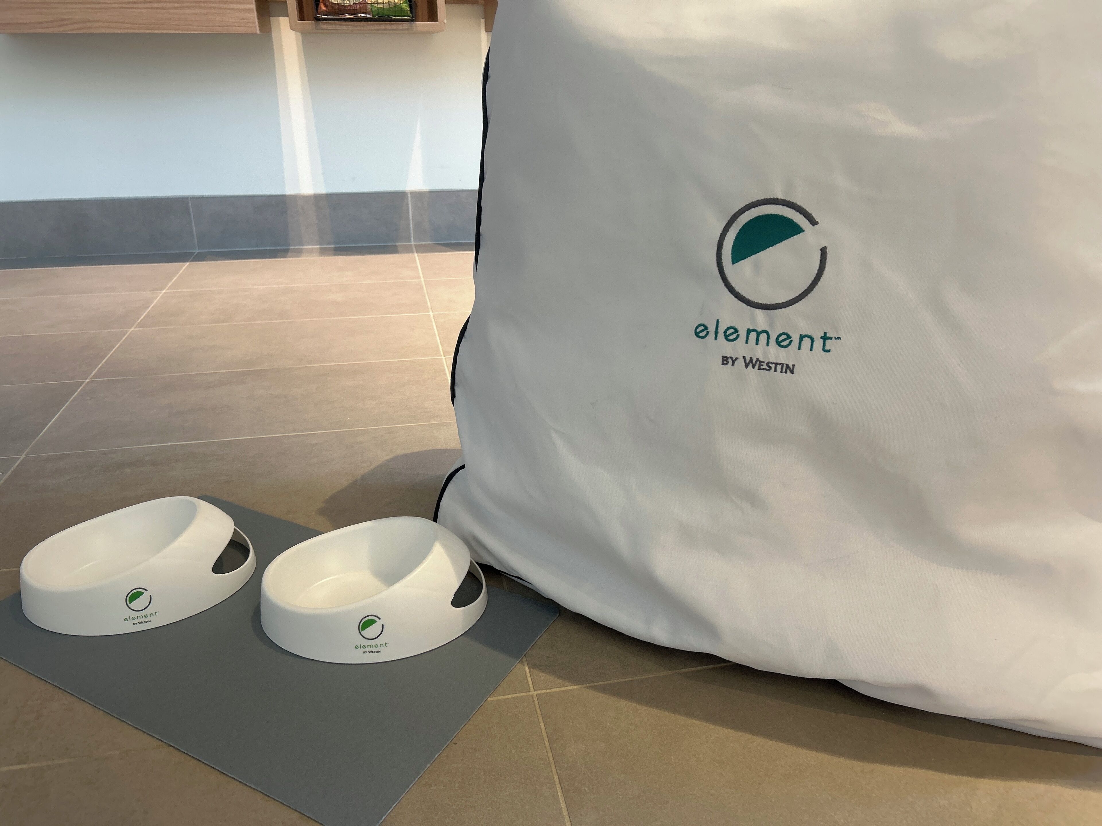 Una borsa bianca con il logo 'element by Westin' e due ciotole bianche con lo stesso logo su un tappetino grigio.