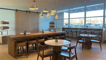 A modern cafe with wooden furniture, large windows, and pendant lighting.