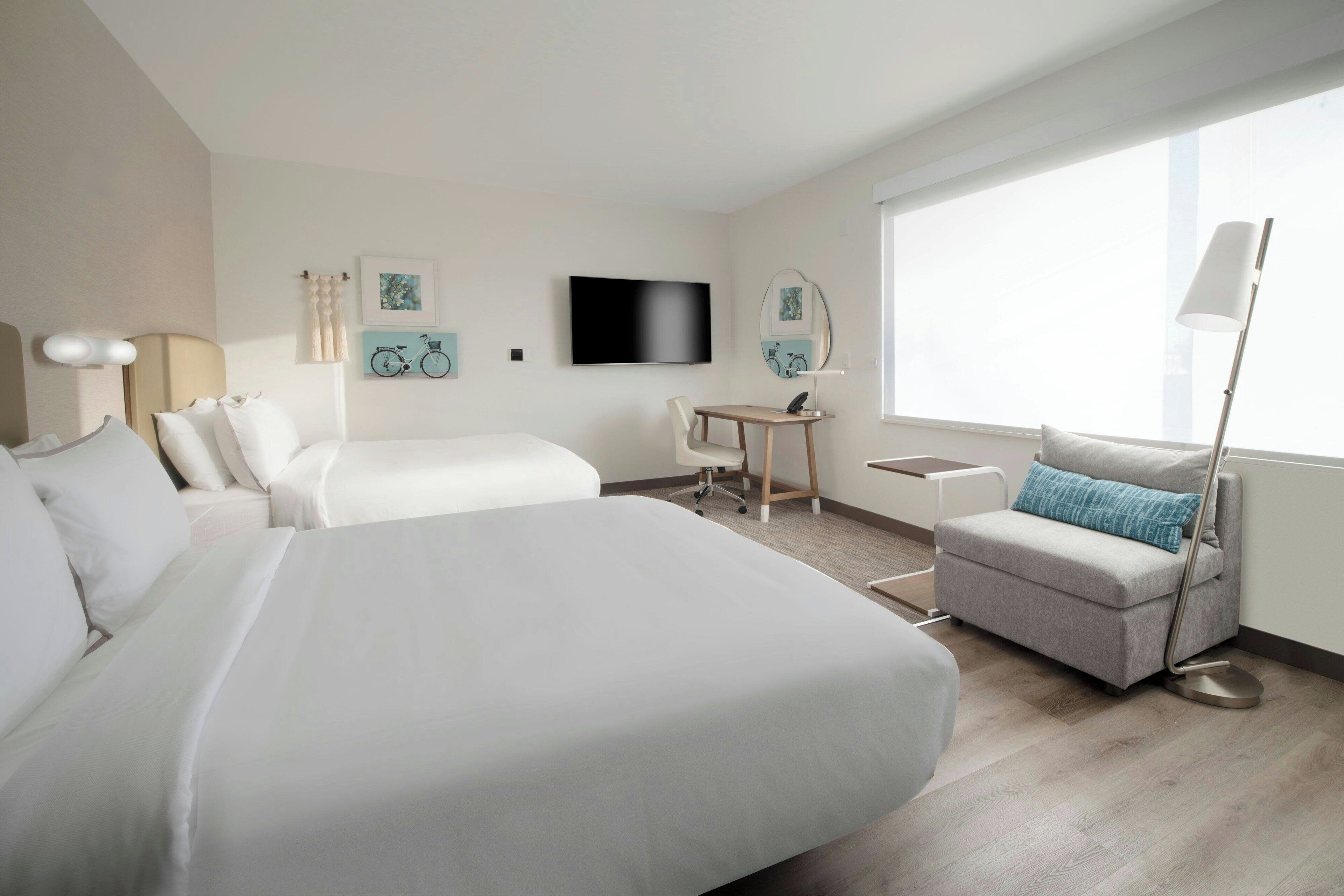 Quarto de hotel moderno com uma cama grande, um sofá, uma escrivaninha e uma televisão.