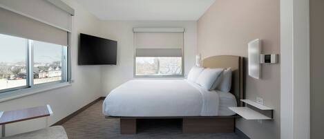 Une chambre d’hôtel moderne dotée d’un grand lit, d’un téléviseur à écran plat fixé au mur, d’une table de chevet et d’une fenêtre offrant une vue sur la ville.