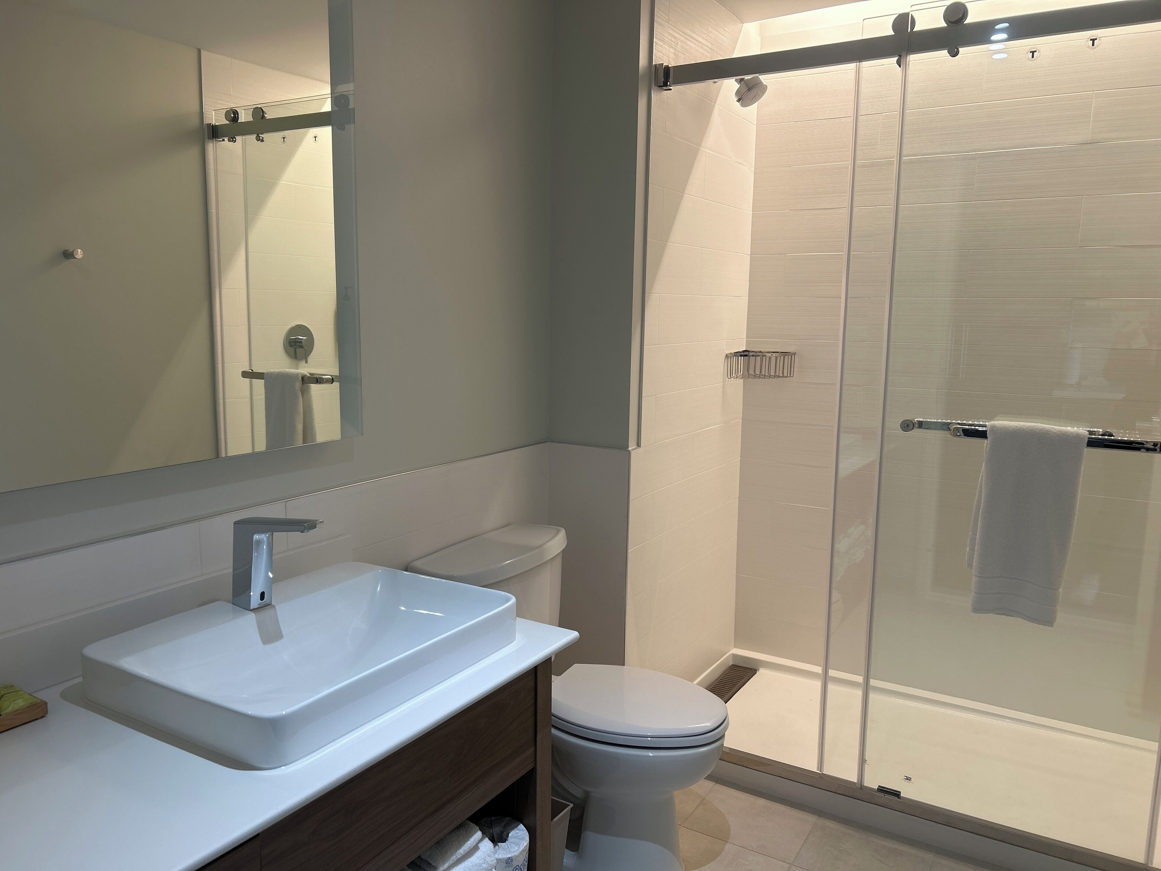 A modern bathroom with a white sink, mirror, toilet, and glass shower enclosure.