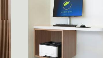 A modern office setup with a flat-screen monitor, keyboard, and mouse on a white desk, and a printer in a wooden cabinet below.