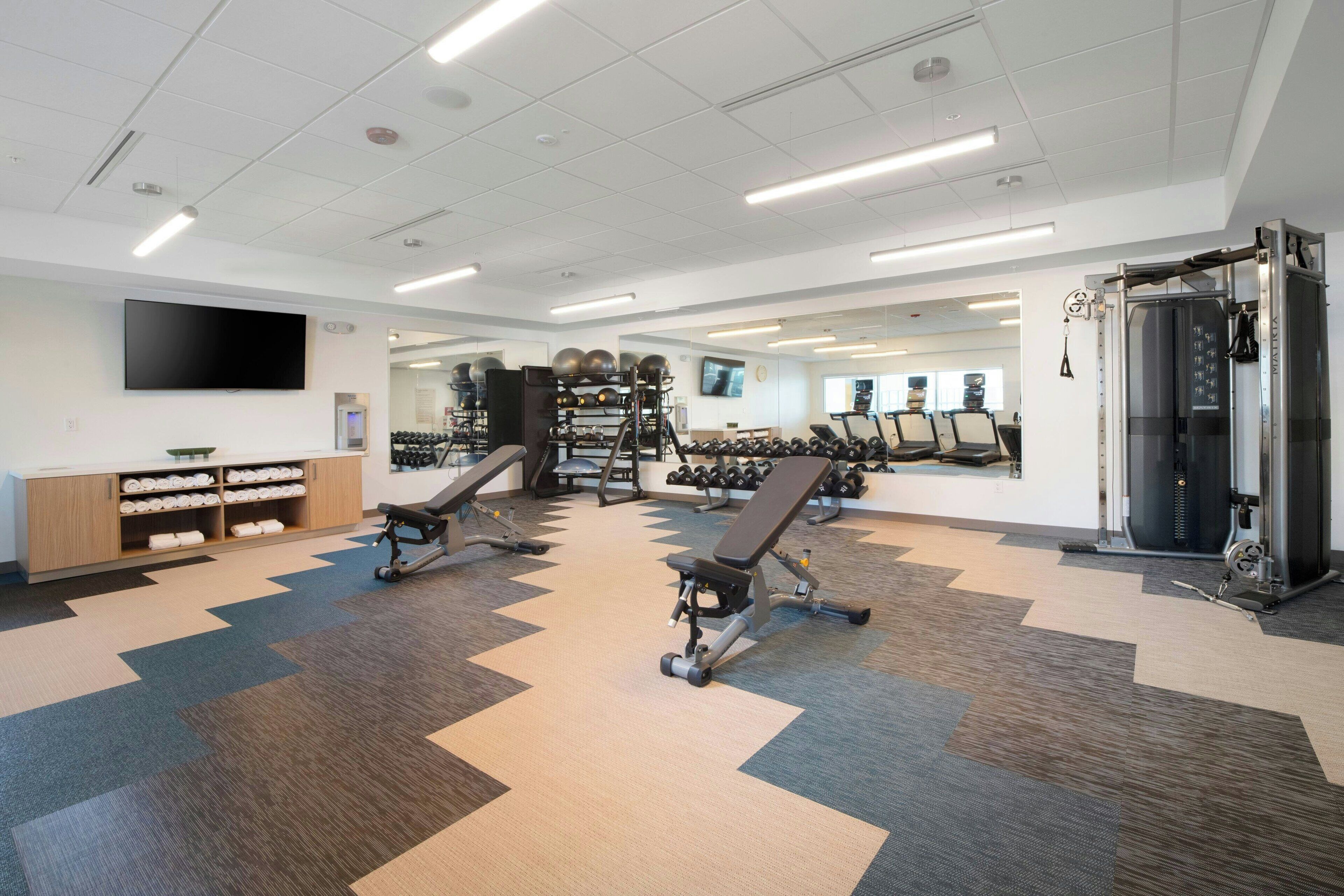 A modern gym with exercise equipment, a television, and a mirrored wall.