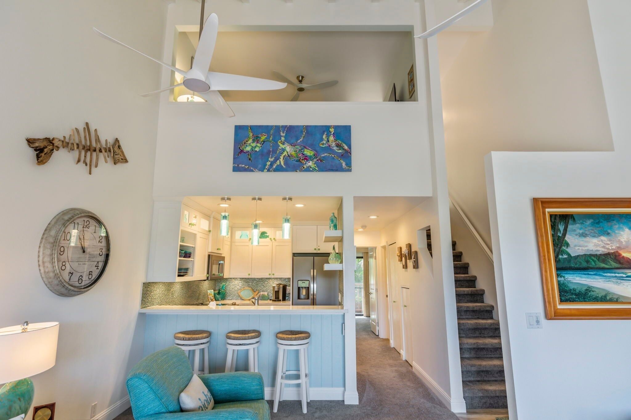 A modern kitchen with a central island, a dining area with a blue sofa, and a staircase leading to an upper level.