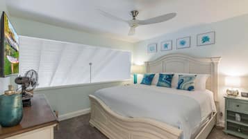 A bedroom with a bed, a ceiling fan, a window with blinds, a desk with a lamp, and a nightstand with a lamp.