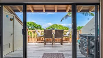 A sliding glass door leading to an outdoor patio with a wooden deck, wicker chairs, and a view of a mountain.
